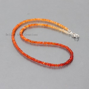 May include: A delicate necklace made with small, round, orange and yellow fire opal beads. The necklace is approximately 18 inches long and has a silver clasp.