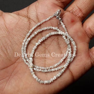 May include: A silver chain necklace made with small, rough, white diamonds. The necklace is on a hand, and the diamonds are clustered together.