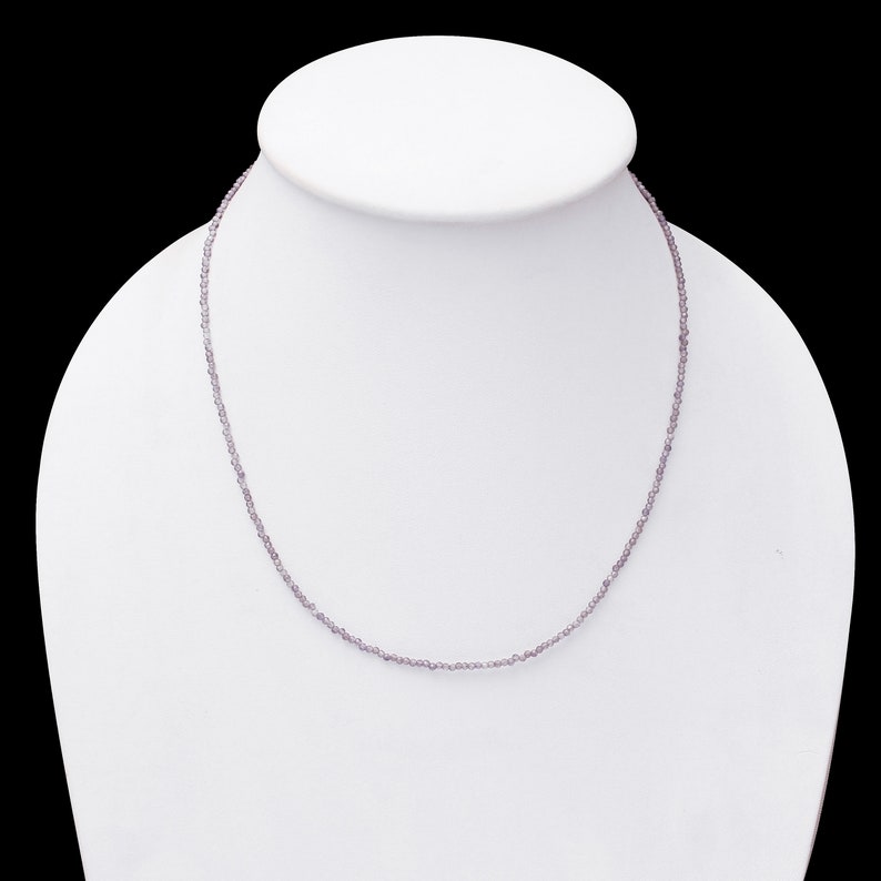May include: A delicate necklace made of small, light purple beads. The necklace is displayed on a white mannequin bust.