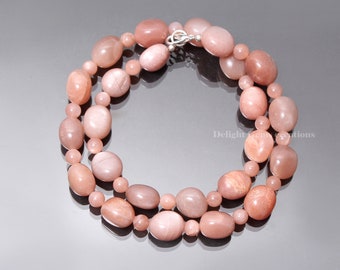 May include: A necklace made of peach-coloured sunstone beads. The beads are oval-shaped and have a shimmery, iridescent finish. The necklace is strung on a silver chain with a lobster clasp.