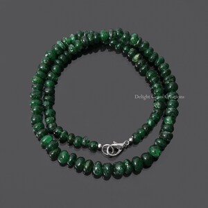 Puede incluir: Un collar compuesto por peque&ntilde;as cuentas redondas de color verde oscuro. Las cuentas est&aacute;n ensartadas, formando un bucle completo con un cierre plateado. El collar se muestra sobre un fondo oscuro.