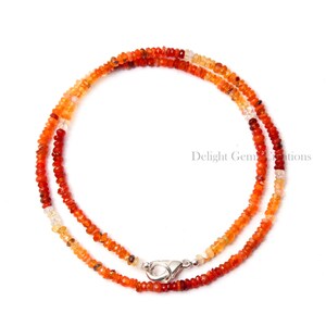Puede incluir: Un collar de piedras preciosas de &oacute;palo multicolor con un cierre de plata. El collar est&aacute; hecho de peque&ntilde;as cuentas redondas que est&aacute;n graduadas en tama&ntilde;o, con las cuentas m&aacute;s grandes en el centro del collar. Las cuentas son una mezcla de naranja, rojo y blanco.