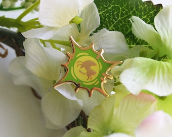 May include: A gold-colored enamel pin with a green background and a stylized image of a bug. The pin is shaped like a starburst and has a white outline.