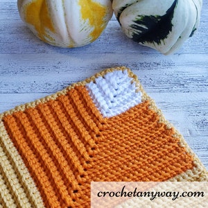 May include: A crocheted square with a candy corn design in orange, yellow and white. The square is made with a textured stitch and has a website address crochetannyway.com in the bottom right corner.