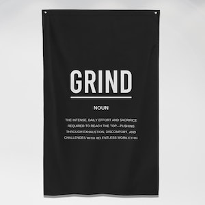 Puede incluir: Pancarta de pared motivacional en blanco y negro con la palabra "GRIND" en letras blancas grandes y una definición de la palabra debajo. La pancarta está colgada en una pared blanca en un entorno de gimnasio con pesas en primer plano.