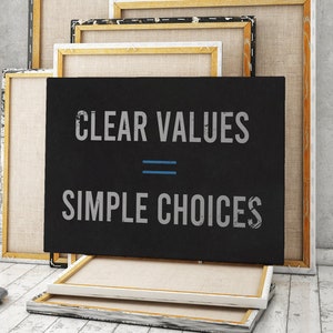May include: A black canvas with the text "CLEAR VALUES = SIMPLE CHOICES" in white lettering. The canvas is leaning against a stack of other canvases in various shades of white and beige.