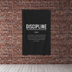 Pu&ograve; includere: Un poster motivazionale in bianco e nero con la parola "DISCIPLINE" in grandi lettere e una definizione della parola sotto. Il poster &egrave; appeso a un muro di mattoni.