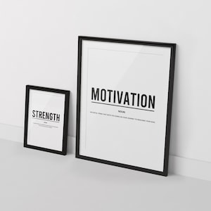 May include: Two black framed prints with white backgrounds and black text. The larger print says "MOTIVATION NOUN The mental drive that gets you going on your journey to reaching your goal." The smaller print says "STRENGTH NOUN The mental or physical power to do something difficult."
