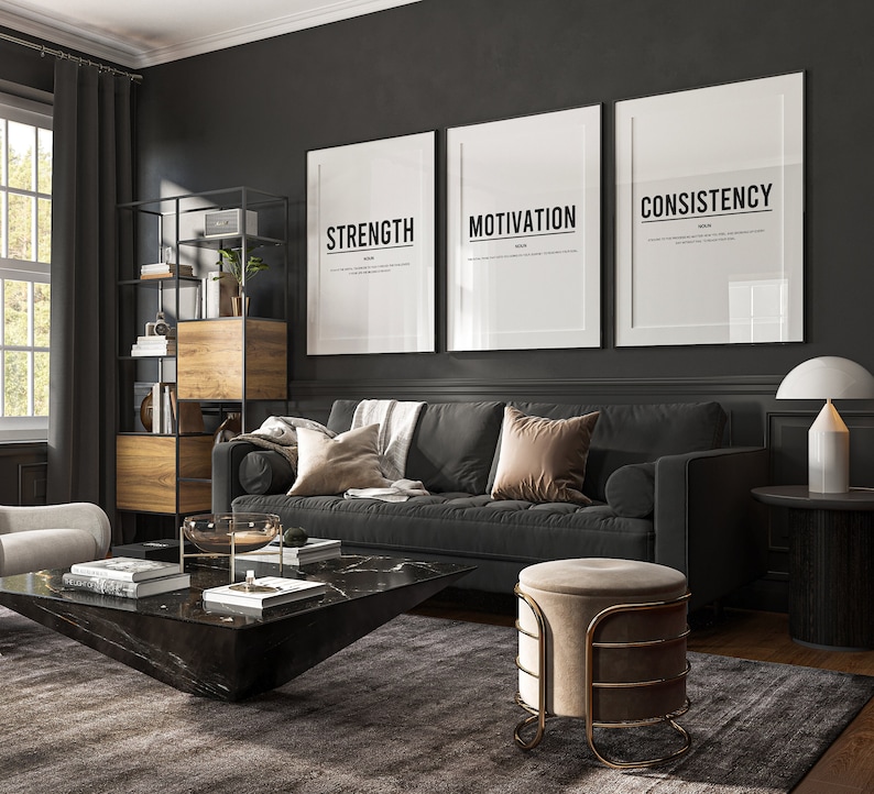 May include: A black leather sofa with three throw pillows, a black coffee table with a marble top, a beige ottoman with a gold metal frame, and three framed prints on the wall with the words "Strength", "Motivation", and "Consistency".
