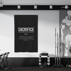Pu&ograve; includere: Un poster motivazionale in bianco e nero con la parola "Sacrifice" in grassetto in lettere bianche. Il poster definisce il sacrificio come "la volont&agrave; di rinunciare al comfort, al tempo e alla facilit&agrave; nella ricerca di qualcosa di pi&ugrave; grande". Il poster &egrave; appeso a una parete bianca in una palestra domestica.