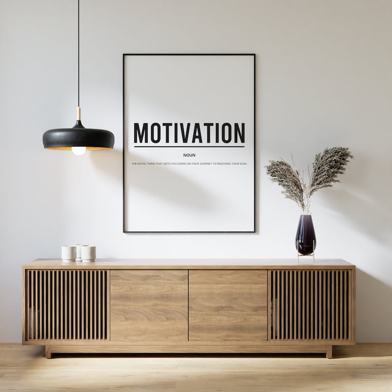 May include: A black and white motivational poster with the word "MOTIVATION" in bold, black letters. The poster is framed in black and hanging on a white wall above a wooden cabinet with two doors. A black pendant light hangs above the cabinet.