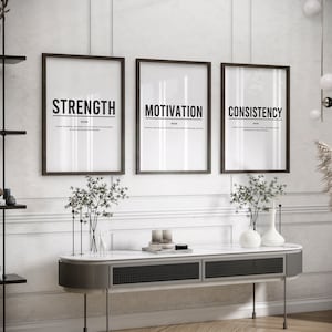 May include: Three black framed prints with white backgrounds and black text. The prints are hung on a white wall and read "Strength", "Motivation", and "Consistency".