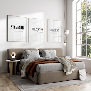 May include: A gray upholstered bed with a brown throw blanket and three framed prints above the headboard. The prints feature the words "Strength", "Motivation", and "Consistency".