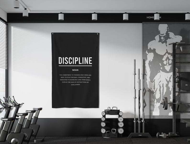 Pu&ograve; includere: Un poster motivazionale in bianco e nero con la parola "DISCIPLINE" in grassetto in lettere bianche. Il poster definisce la disciplina come "l'impegno per allenare la mente e il corpo per rimanere concentrati, coerenti e dedicati al raggiungimento di obiettivi a lungo termine, anche di fronte a distrazioni o sfide."