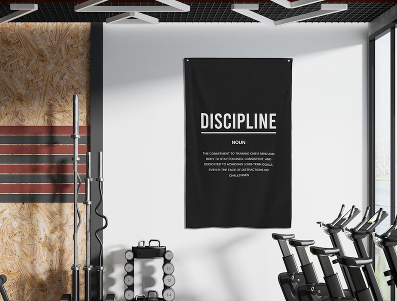 Pu&ograve; includere: Un poster motivazionale in bianco e nero con la parola "DISCIPLINE" in grandi lettere bianche. Il poster definisce la disciplina come "l'impegno di allenare la mente e il corpo per rimanere concentrati, coerenti e dedicati al raggiungimento di obiettivi a lungo termine, anche di fronte a distrazioni o sfide."