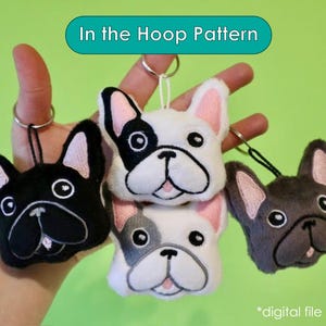 May include: Three plush French bulldog keychains in black, white, and gray. The keychains are hanging from a hand. The text "In the Hoop Pattern" is at the top of the image.