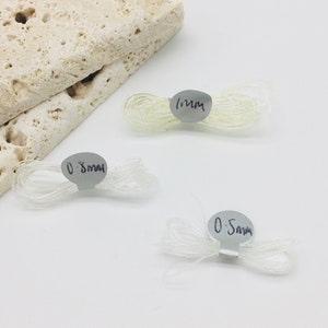 May include: Three spools of clear elastic thread, labelled with their thickness in millimetres: 0.5mm, 0.8mm, and 1mm.
