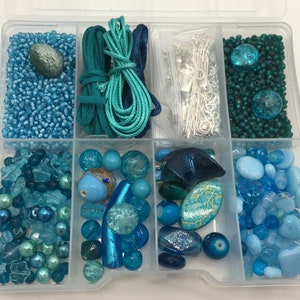 May include: A clear plastic storage box filled with various shades of blue and teal beads, glass pieces, and cord. The box is divided into 10 compartments.