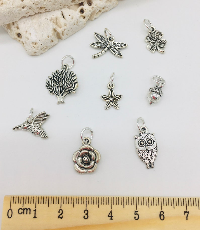 Peut inclure: Un ensemble de huit breloques en argent avec des motifs inspir&eacute;s de la nature, notamment une libellule, un tr&egrave;fle &agrave; quatre feuilles, un arbre, une fleur, un gland, un colibri, une rose et un hibou.