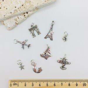 Peut inclure: Un ensemble de neuf breloques en argent avec des motifs sur le th&egrave;me du voyage, notamment un avion, un croissant de lune avec des &eacute;toiles, une &eacute;toile, un voilier, un avion, la tour Eiffel, l'Arc de Triomphe et un croissant de lune.