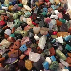 May include: A selection of mixed gemstone beads in diverse shapes and colours, including red, blue, green, and purple. The beads are tumbled and polished, with holes for stringing. Gemstones include quartz, turquoise, and amethyst.