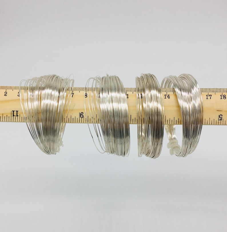 May include: A close-up of a ruler with six spools of silver wire wrapped around it. The ruler is marked in inches.