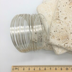 May include: A stack of 25 silver-colored wire rings, each approximately 1/4 inch wide, arranged in a circle. A ruler is visible in the bottom of the image, showing the rings are about 6 inches in diameter.