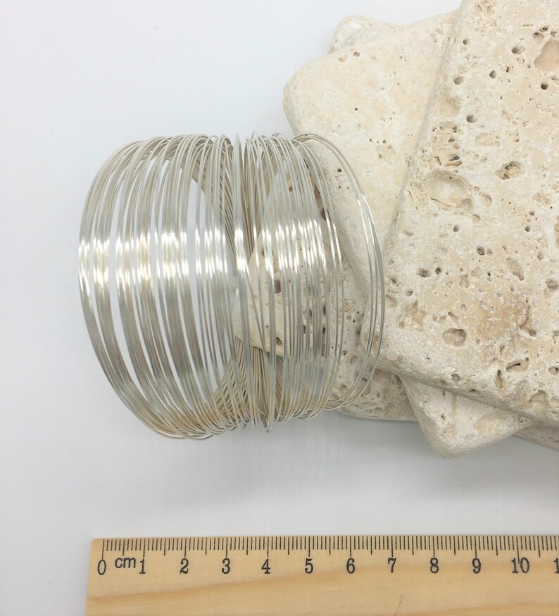 May include: A stack of 25 silver-colored wire rings, each approximately 1/4 inch wide, arranged in a circle. A ruler is visible in the bottom of the image, showing the rings are about 6 inches in diameter.