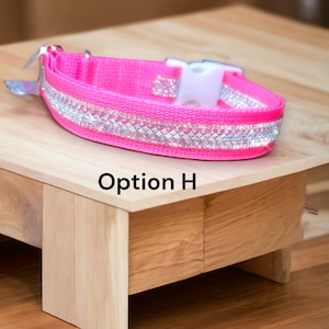 Pode incluir: Uma coleira rosa brilhante para cães com uma faixa de strass prateados. A coleira tem uma fivela de plástico branco e um fecho de metal prateado. O texto "Option H" está impresso na superfície de madeira.