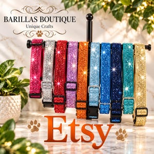 Può includere: Una collezione di dieci collari glitterati per animali in vari colori tra cui rosa, argento, rosso, viola, arancione, azzurro, blu, blu scuro, verde acqua e oro, appesi a un espositore in metallo nero con fibbie e clip regolabili.