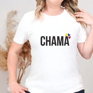 Pu&ograve; includere: Una t-shirt bianca a maniche corte con la parola CHAMA stampata in grassetto nero a lettere maiuscole sul petto. Sopra la lettera A, si trova un piccolo elemento grafico composto da quattro icone a forma di cuore di colore giallo, blu e rosso.