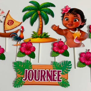 K&ouml;nnte beinhalten: Ein Set aus Tortensteckern mit einem Cartoon-Baby, einem Schwein, einem Hahn, einem Segelboot, einer Palme und mehreren rosa Hibiskusbl&uuml;ten auf wei&szlig;en St&auml;bchen. Ein rechteckiges Schild in Holzoptik zeigt den Namen JOURNEE in glitzernden Buchstaben.