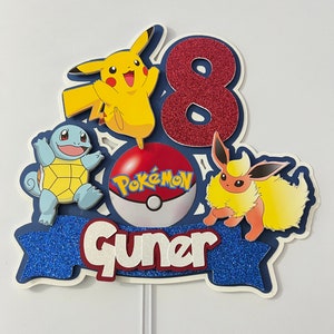 K&ouml;nnte beinhalten: Ein blauer und roter Tortendekor mit einer roten Zahl 8, einem gelben Pikachu, einem blauen Squirtle, einem braunen und gelben Eevee und einem roten Pok&eacute;ball mit dem Wort "Pok&eacute;mon" darauf. Der Dekor hat auch ein blaues Banner mit dem Wort "Guner" darauf.
