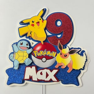 K&ouml;nnte beinhalten: Ein blauer, roter und gelber Pokemon-Kuchentopper mit einer roten Nummer 9, einem gelben Pikachu, einem blauen Squirtle, einem gelben Eevee und einem roten Pokeball mit dem Wort "Pokemon" darauf. Der Topper hat auch ein blaues Banner mit dem Namen "Max" darauf.