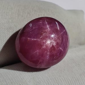 May include: A cabochon cut, star ruby gemstone with a deep red color and a six-rayed star.