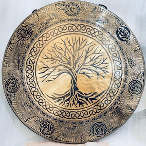 May include: A large, round, gold-colored gong with a black tree of life design in the center. The gong is decorated with a black Celtic knot border and black floral patterns around the edge.