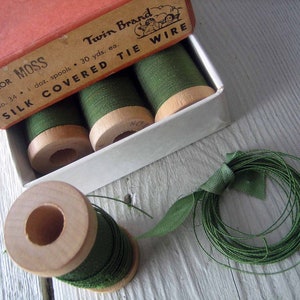 May include: A box of green silk covered tie wire, labeled "Color Moss Twin Brand No. 34 1 doz. spools 30 yds. ea. Silk Covered Tie Wire". The box is open and there are three spools of wire inside. There is also a spool of green wire outside the box.