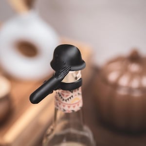 Stålhjälm med arm som dryckesskydd för öl, läsk och små champagneflaskor. Skyddar din dryck från insekter och droger mot våldtäkt.