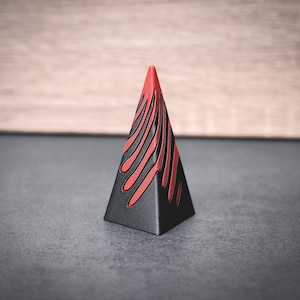 Puede incluir: Un objeto negro con forma de pirámide con rayas rojas en la superficie.