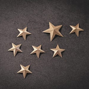 May include: Seven gold star-shaped ornaments on a black background.