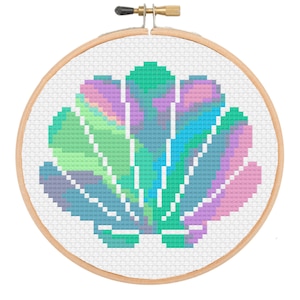 May include: A cross-stitch pattern of a seashell with a rainbow of colours, including pink, blue, green, and purple. The seashell is stitched on white Aida cloth and is framed in a wooden embroidery hoop.