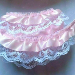 May include: Pink satin ribbon with white lace trim. The ribbon is ruffled and has a delicate, feminine look.
