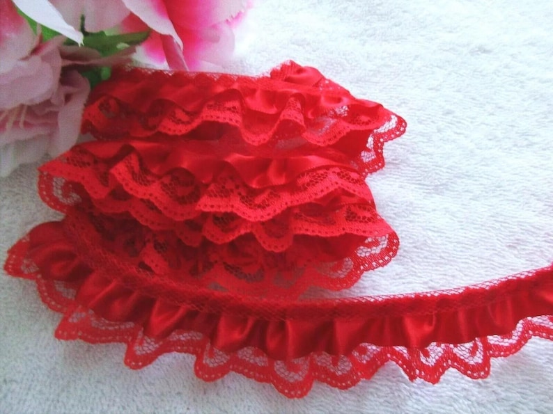 May include: Red lace trim with a ruffled satin edge. The trim is layered and has a scalloped edge.