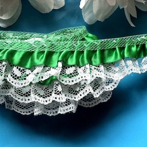 May include: Green satin ribbon trim with white lace edging. The ribbon has a ruffled edge and the lace has a scalloped edge.