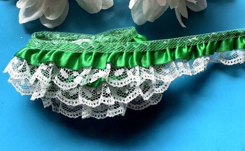 May include: Green satin ribbon trim with white lace edging. The ribbon has a ruffled edge and the lace has a scalloped edge.