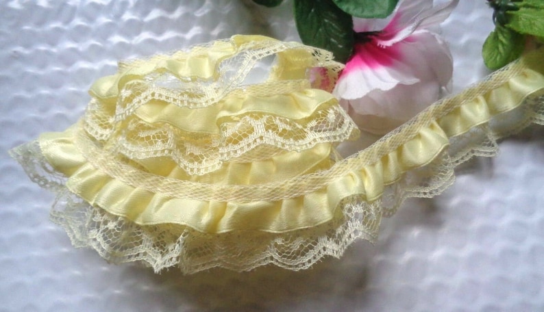 May include: Yellow ruffled lace trim with a satin ribbon. The trim is layered and has a delicate, feminine look.