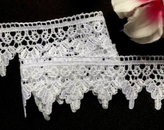 May include: White lace trim with a scalloped edge. The lace has a delicate floral pattern.