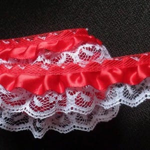 May include: Red satin ribbon trim with white lace edging. The trim has a ruffled look and is perfect for adding a touch of elegance to any project.