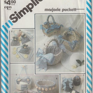 May include: Simplicity sewing pattern featuring various decorative baskets and containers. The designs include woven baskets, boxes, and round containers, adorned with bows, floral accents, and lace trim. The pattern includes the text "marjorie puckett" and the number "5743".