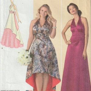 Könnte beinhalten: Simplicity Schnittmuster Nummer 1406 AA für ein Halstuchkleid mit einem hoch-tiefen Saum. Das Schnittmuster beinhaltet zwei Kleidvarianten: eine mit Camouflage-Druck und rotem Saum und die andere mit einfarbigem rosa Stoff. Das Schnittmuster ist für die Größen US 10-18, Euro 36-44 und Französisch 38-46.